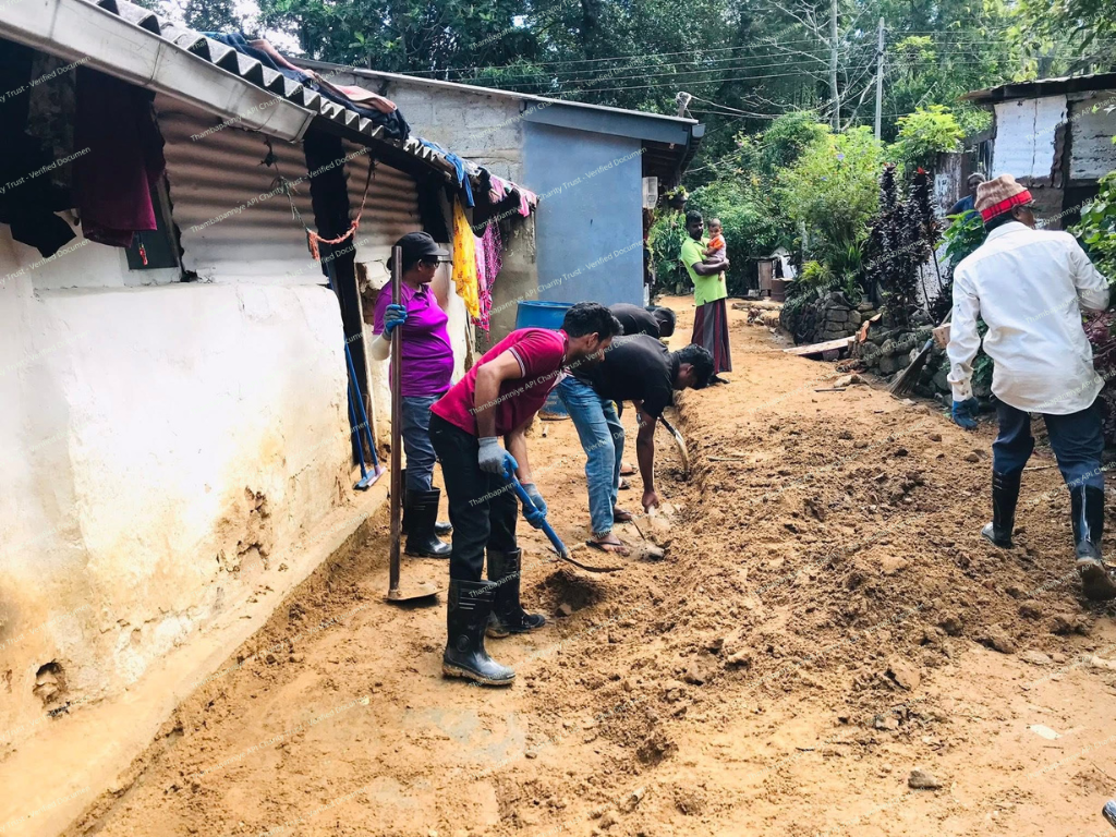 Villagers clearing mud along the outside wall of a home